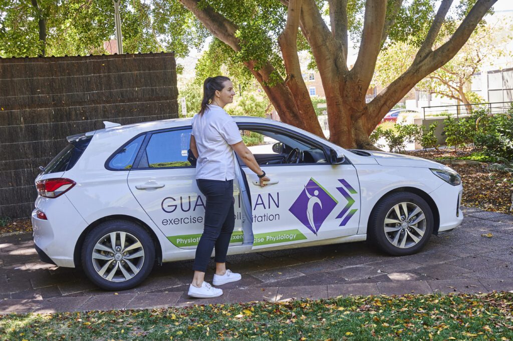 Home A woman stands beside a car displaying a sign, symbolizing her journey in exercise rehabilitation.
