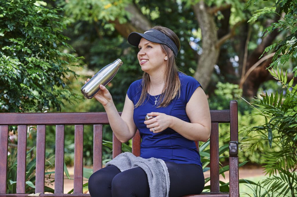 Benefits Of Healthy Weight Loss A woman, an exercise physiologist, sits on a bench, holding a water bottle, enjoying a moment of rest after her workout.