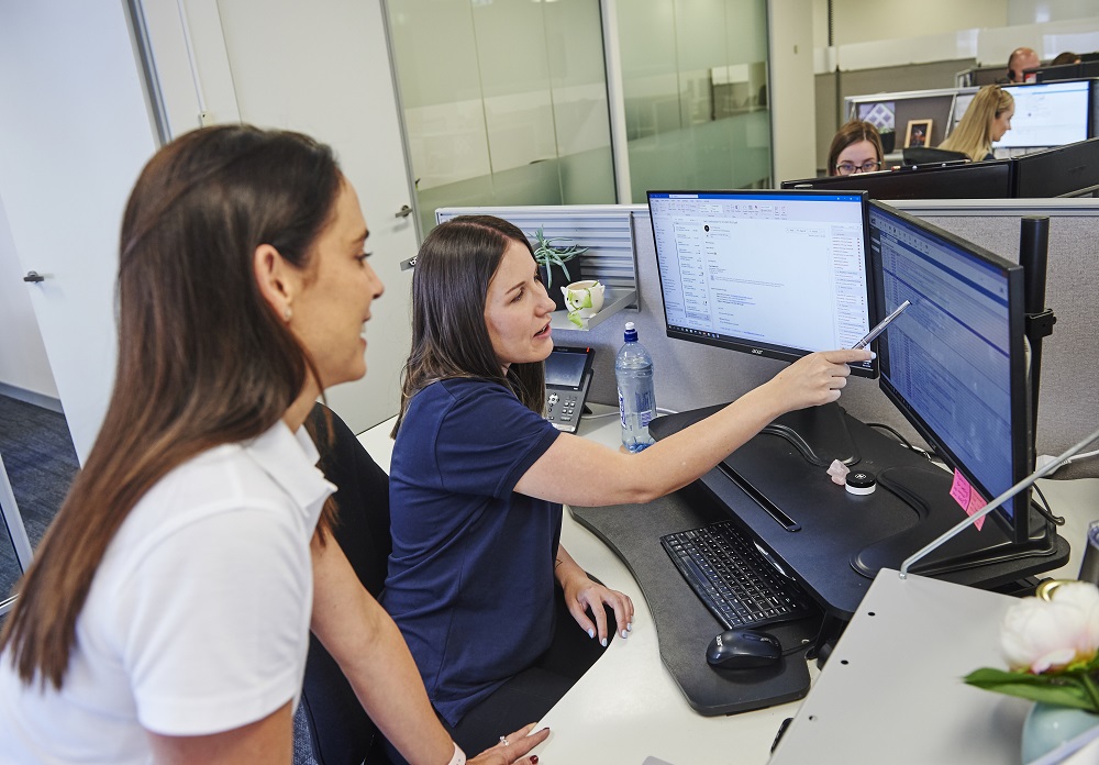 Two women collaborate on a computer in an office, showcasing teamwork at Guardian Exercise Rehabilitation careers.